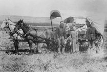 A family during the Great Western Migration, 1866, stands alongside their covered wagon.