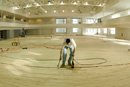 Hit the court. The new four-court basketball facility in the Fitness and Recreation Center, which opens this spring, is designed also for volleyball and badminton competition. It features a one-eighth-mile running track suspended near its ceiling. A worker from Kenvo Floor Company, of Exeter, R.I., lays down the hardwood surface on November 16. Photo by Vernon Doucette