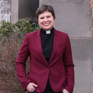 Headshot of Jessica in a maroon blazer and clergy collar. Photo taken outdoors