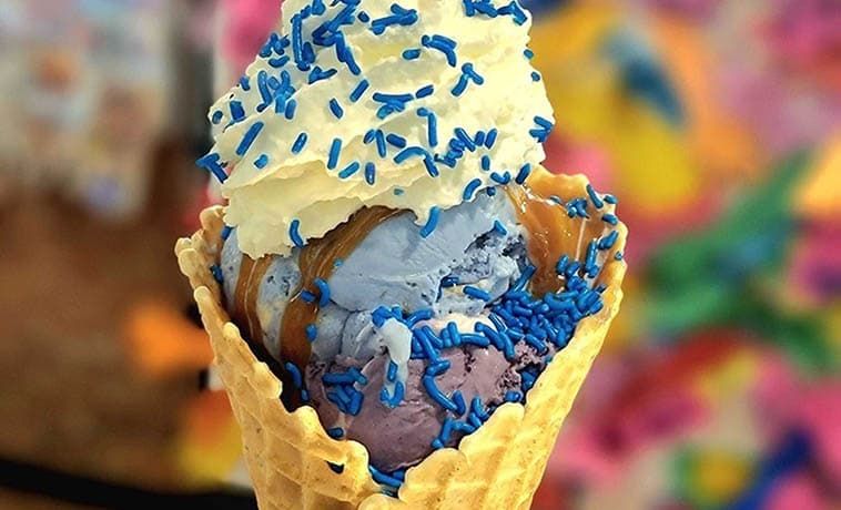 Blue and purple ice cream with whipped cream and blue sprinkles in a waffle cone.