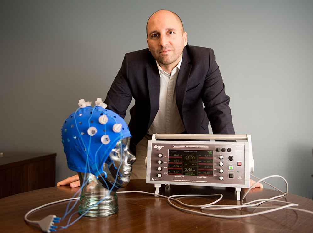 Portrait of Rob Reinhart, assistant professor of psychological and brain sciences at Boston University, posing with an electrstimulation device that he uses in his research.