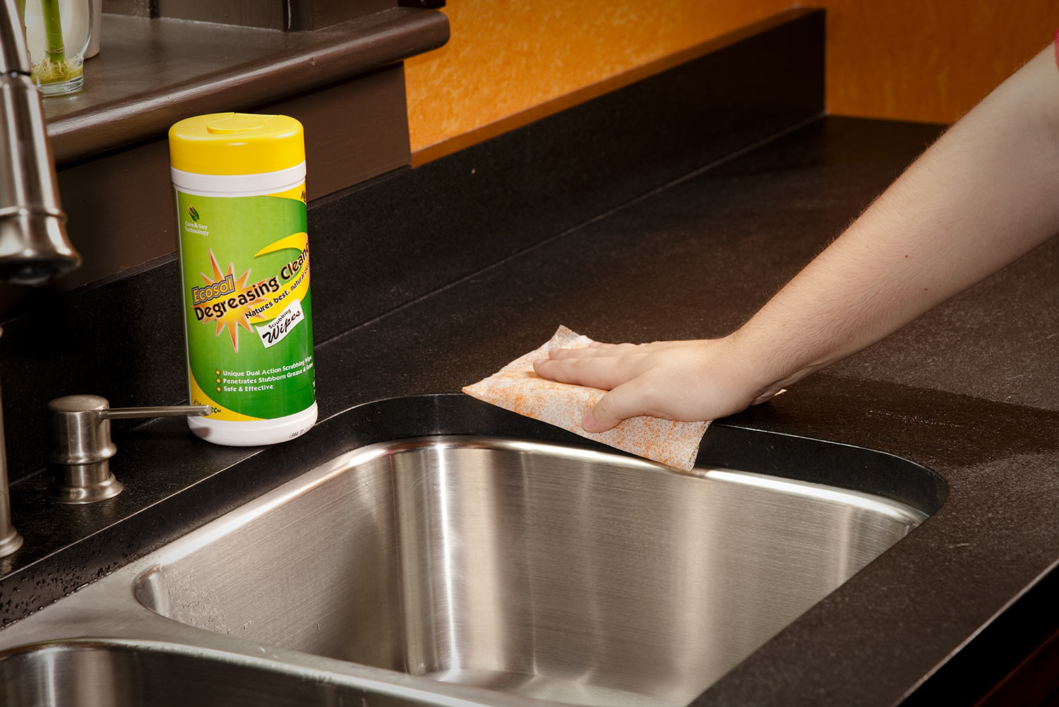 A hand wipes a kitchen sink with a disinfecting wipe.