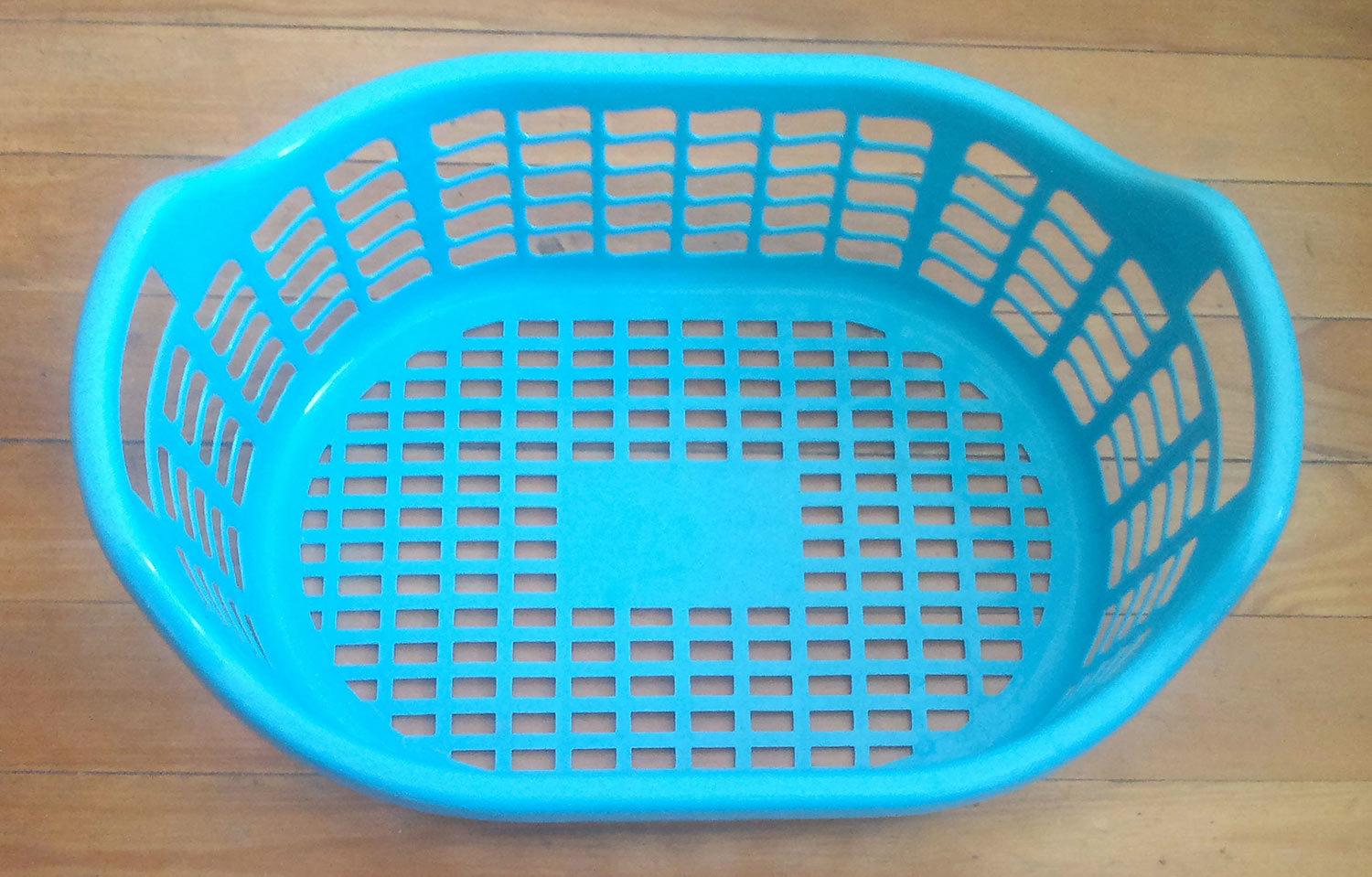 Empty light blue plastic laundry basket sitting on a wood floor.