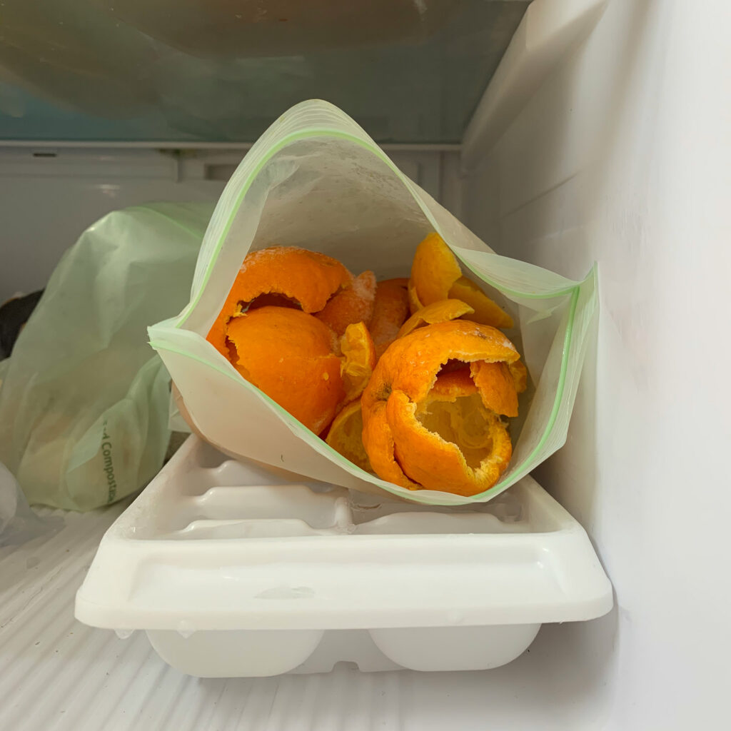 Pile of citrus peels in a plastic bag in the freezer on top of an ice cube tray.