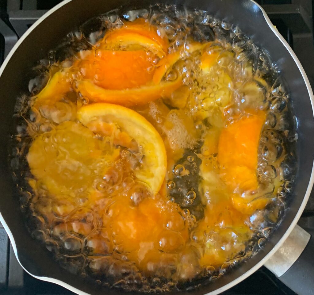 Photo of oranges being blanched in a sauce pan taken from above. The liquid in the pan is at a heavy boil.