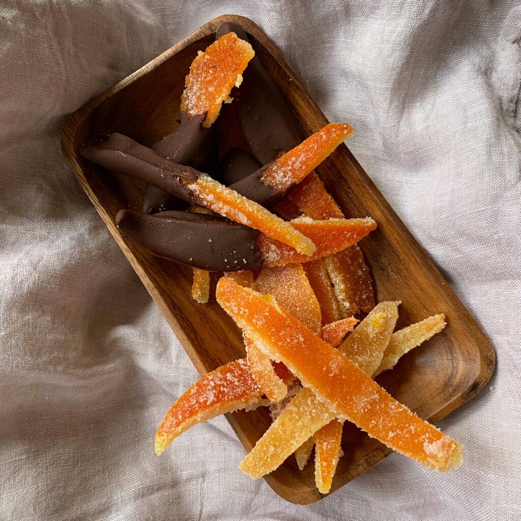 Candied orange peels and chocolate candied orange peels in a oblong wooden bowl on a linen cloth.