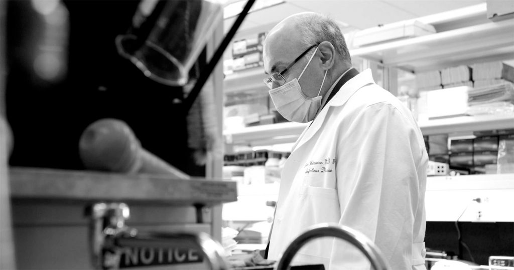 Black and white photo of Weissman wearing a facemask and working in his lab. Weissman is working on a pan-coronavirus vaccine—one that will protect against every variant that will likely appear—as well as about 20 other vaccines for diseases from malaria to HIV.