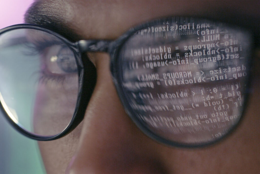 Photo: Closeup of code text reflecting off the glasses of someone looking at a computer screen