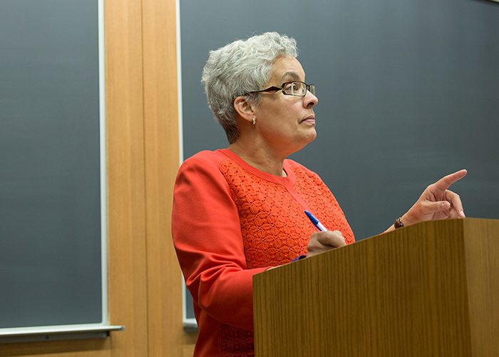Professor Maria O'Brien in a tangerine top lecturing students in front of a blackboard
