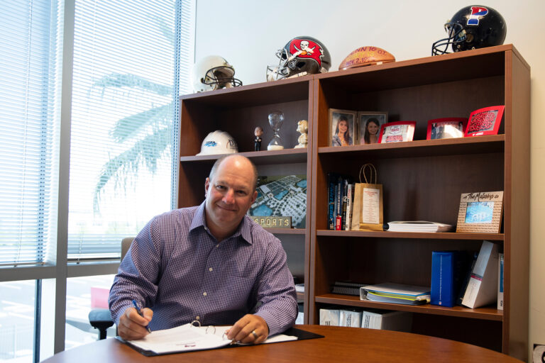 dan malasky tampa bay buccaneers in his office with an impressive display of helmets, trophies and books behind him.