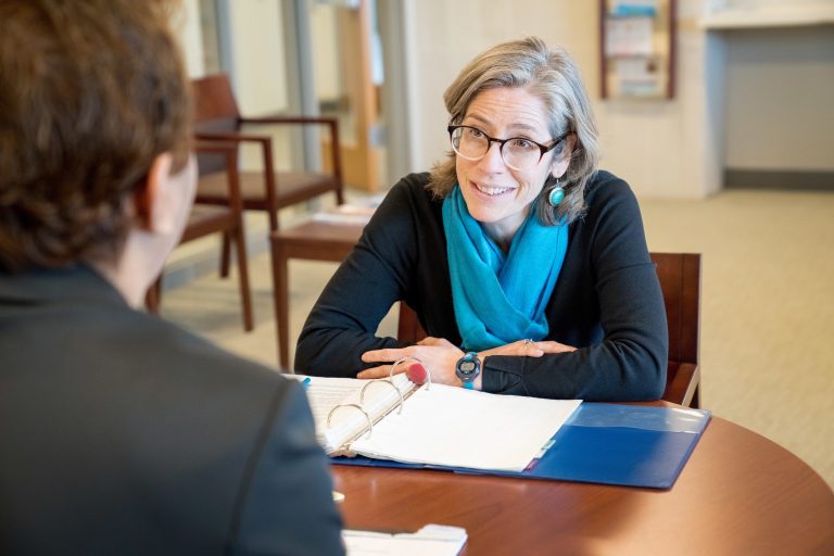 LAW advisor in bright teal scarf and glasses engaging a student over open files