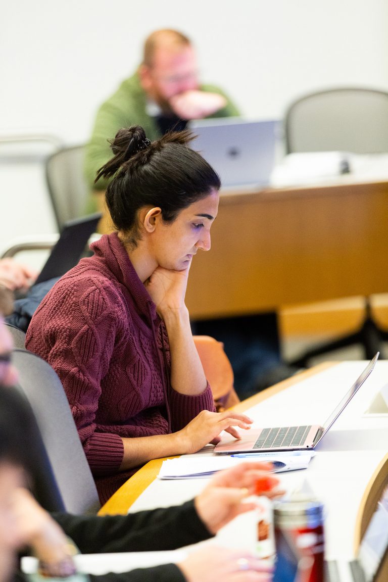 Student gazes intently at her laptop in a burgundy button up in a lecture hall