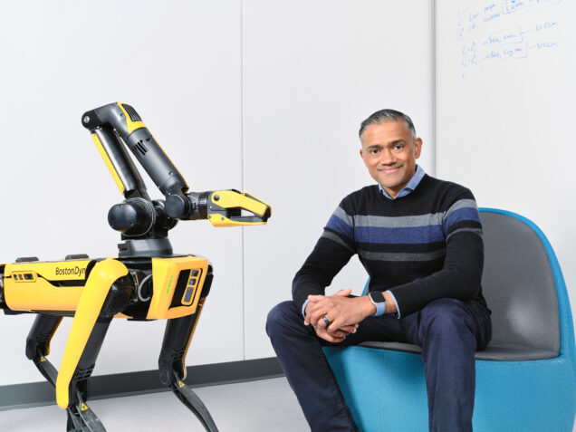 Vasanth Sarathy ('10) sits in a blue chair with a robot next to him