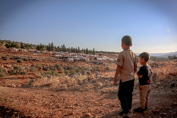 Immigration and human rights law at BU Law. Two children standing while looking at refugee camp in the distance.
