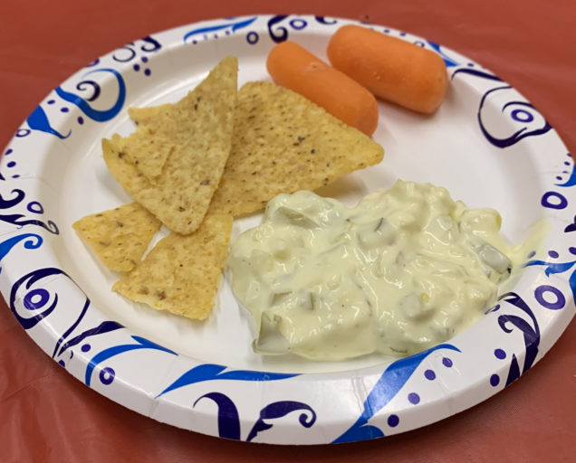 To show dill pickle dip being served along with tortilla chips and carrots.