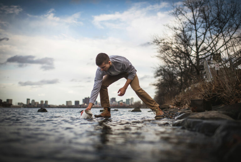 Photo of researcher collecting a sample out of a body of water.
