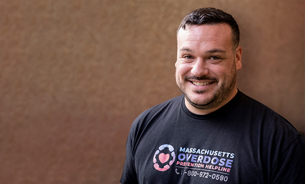 Headshot of Stephen Murray wearing a t-shirt that reads "Massachusetts Overdose Prevention Helpline 1-800-972-0590"