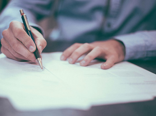 photograph of a person's hands holding a pen and reviewing paperwork