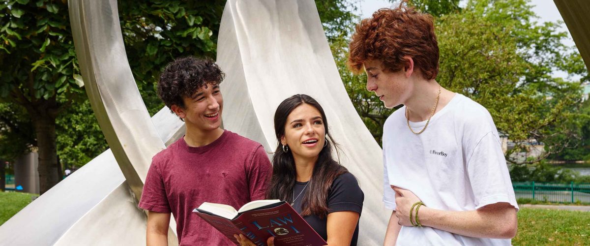 Boston University students consult a law book while sitting on a statue