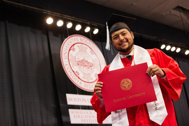 BU Wheelock graduate smiles with his diploma walking across stage