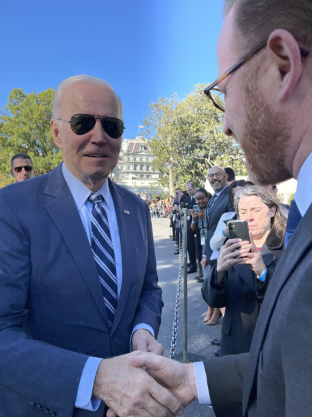 President Joe Biden on the left in sunglasses reaching hand out to shake the hands oof Josh Goodman