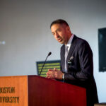 Photo: A picture of a man in a dark suit speaking at a podium. On the podium are the words "Boston University"