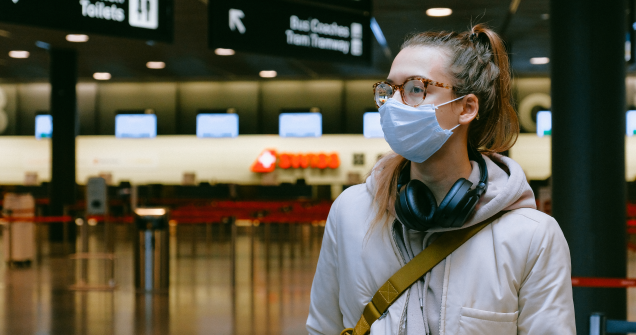 a girl in a mask stands alone in an empty airport