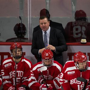 BU men's ice hockey head coach Albie O'Connell talks to a player on the bench during a game.