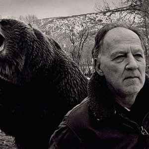 Werner Herzog with a grizzly bear roaring behind him, in grayscale