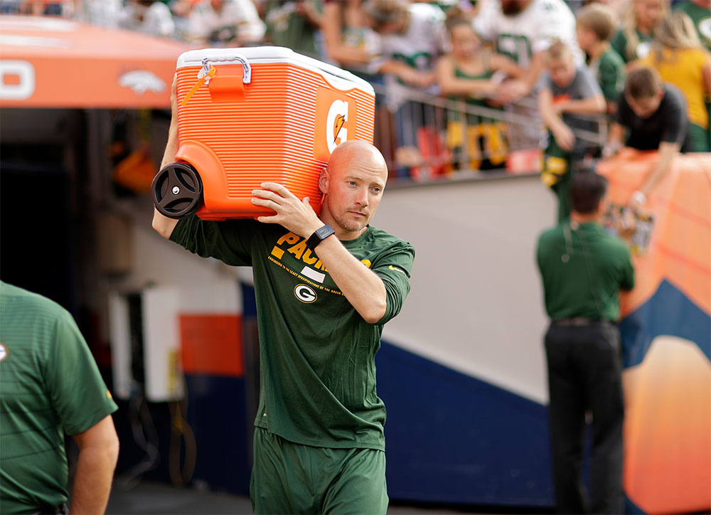 Sports dietitian Adam Korzun carries an orange cooler while walking the sidelines during a Green Bay Packers game.