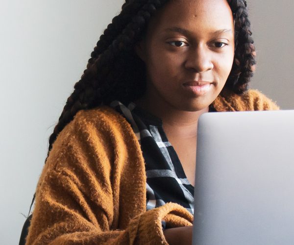 A black woman sits at an open laptop.