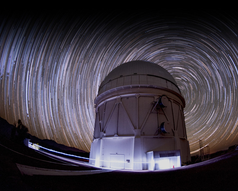 The double door on the ground level of the telescope dome provides a sense of scale (Figure 6). Just inside those doors is a control room from which the camera and telescope are operated each night. Four stories up sits the base of the telescope. The dome is a few stories tall and is covered with aluminum sheets to reflect sunlight during the day. For observations, a large slit, located to the right of the dome, retracts after sunset to allow the telescope and camera to see the night sky. The dome rotates depending on which way the telescope is aimed. The Blanco telescope is probably most famous for its use in the discovery of cosmic acceleration in 1998 by two teams of scientists who studied supernovae in distant galaxies. The 2011 Nobel Prize in physics was awarded to Saul Perlmutter, Adam Riess, and Brian Schmidt for this discovery.