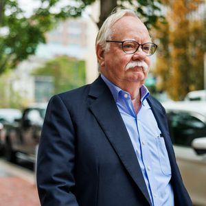 Robert A. Brown, President Emeritus stands alongside Commonwealth Ave. The weather is overcast. He appears to be focused.