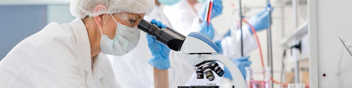 woman in PPE looking in a microscope