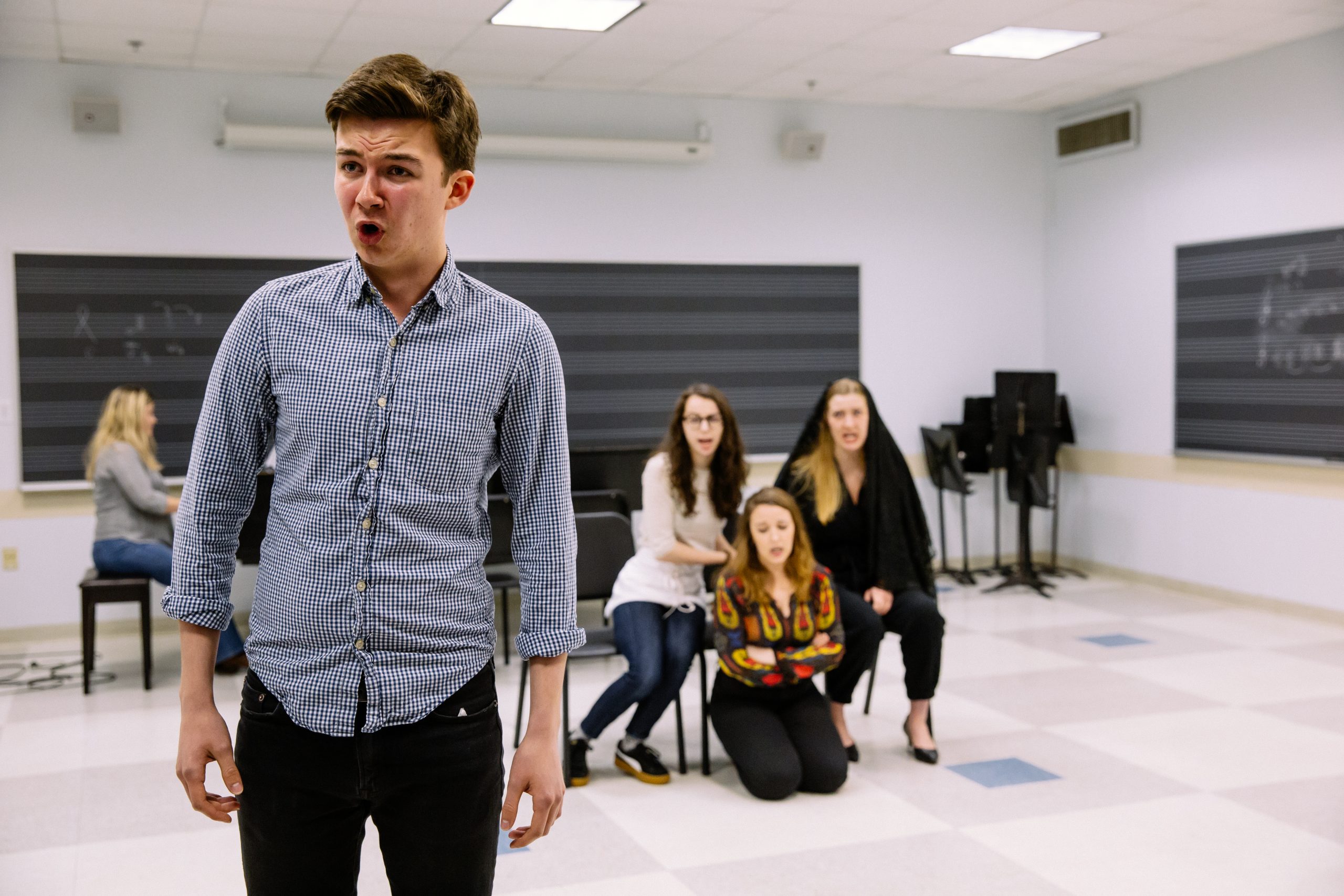 Student singing in front of classmates, additional singers in the background