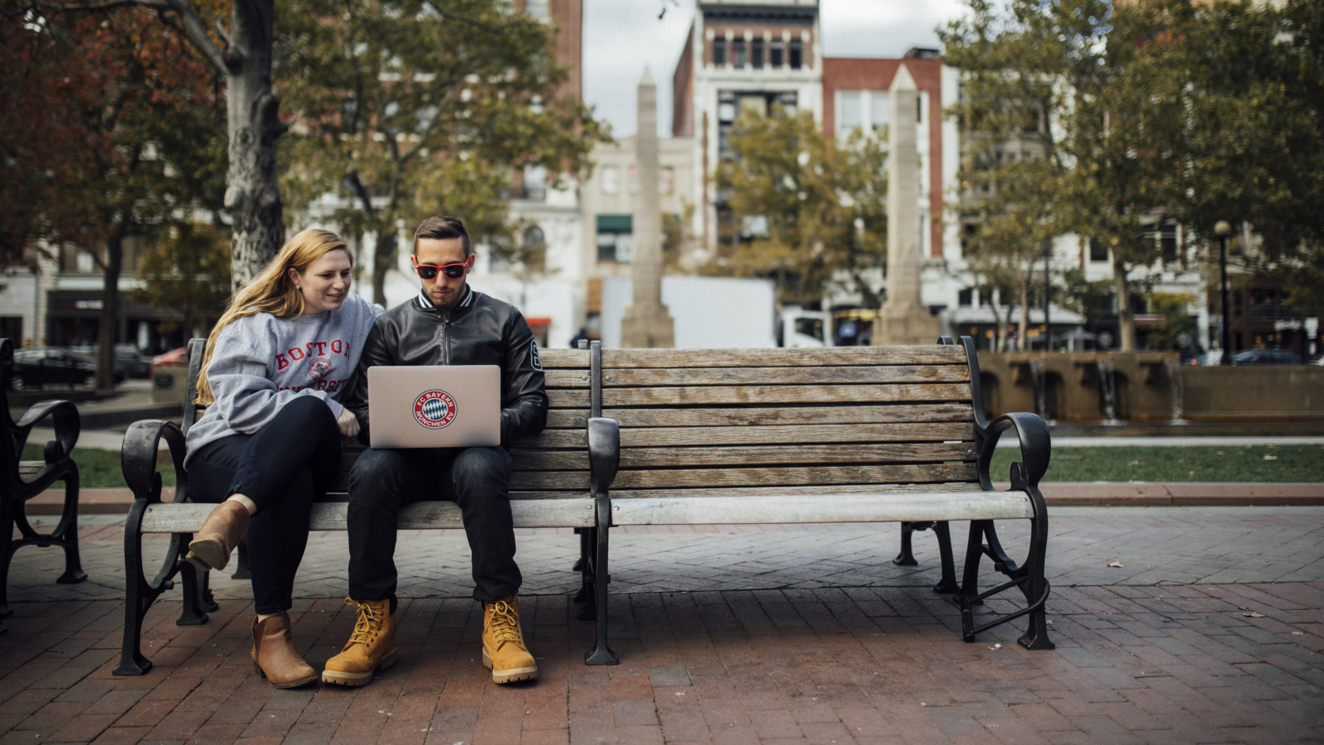 Two BU students sitting on a park bench with their laptop