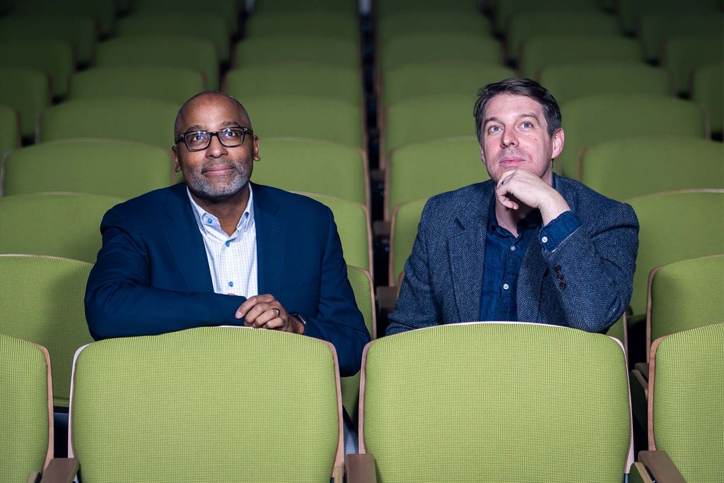 Film scholars and aficionados Harvey Young, dean of the College of Fine Arts (left), and Jonathan Foltz, a College of Arts & Sciences assistant professor of English and program director of its Cinema & Media Studies program, looking up at a film screen while sitting in an empty theatre with bright green seats. 