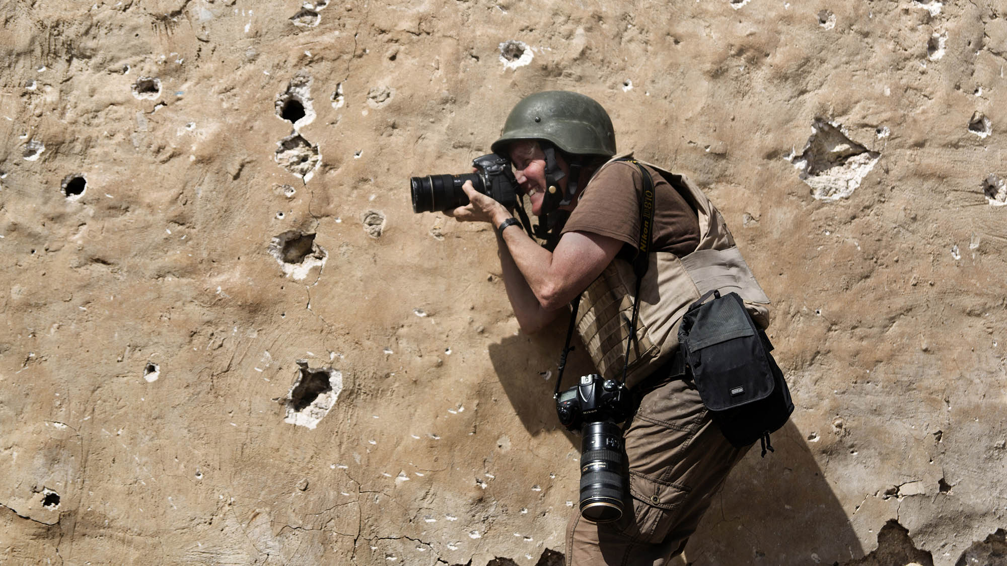 Carol Guzy taking photos while dressed in fatigues and wearing a helmet