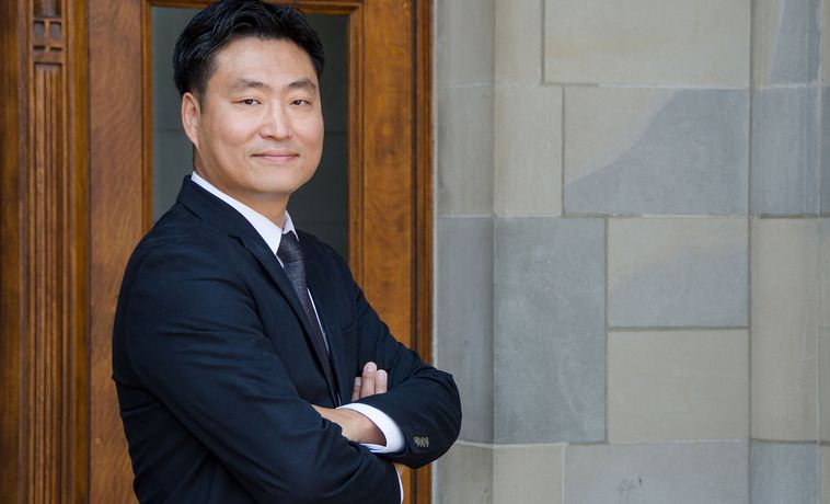 Sun Un Yang poses in dark suit with his arms crossed.