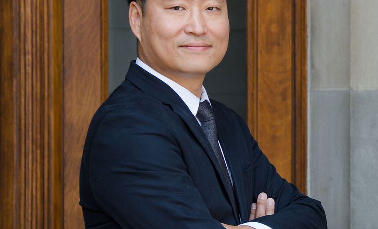 Sun Un Yang poses in dark suit with his arms crossed.