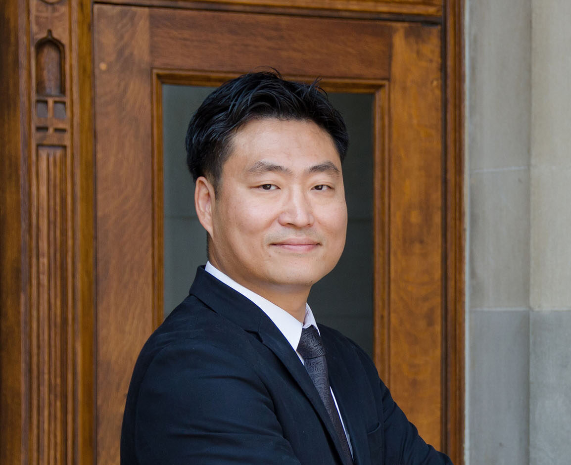 Sun Un Yang poses in dark suit with his arms crossed.