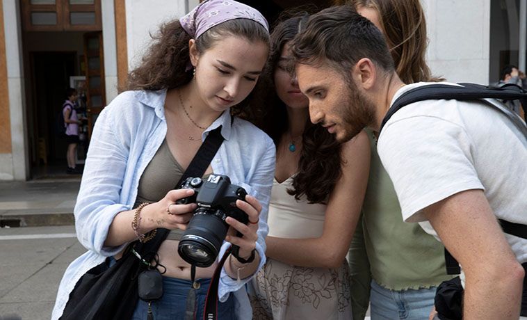 Four student photo journalists gather to look at images on the rear screen of a digital camera while on assignment in Italy..