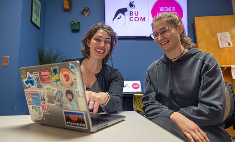 Two women working at a desk with a laptop.