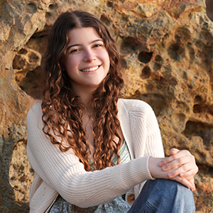 A joyful photo of Ellie Posen sitting in front of rocks.