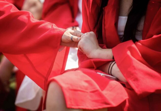 Detail photo of two graduates holding hands during Commencement.