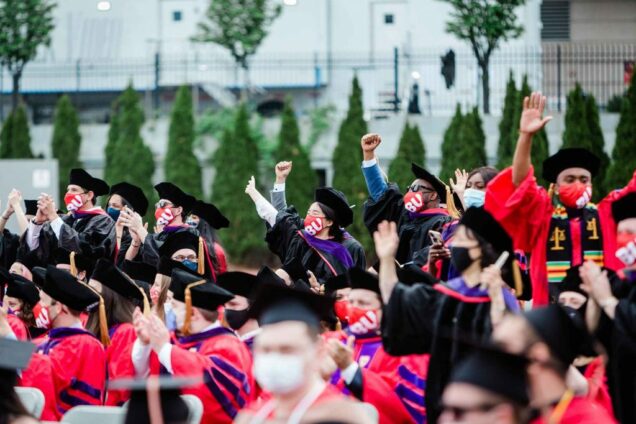 Graduating doctoral students hold their hands in the air and cheer during BU's 148th Commencement.