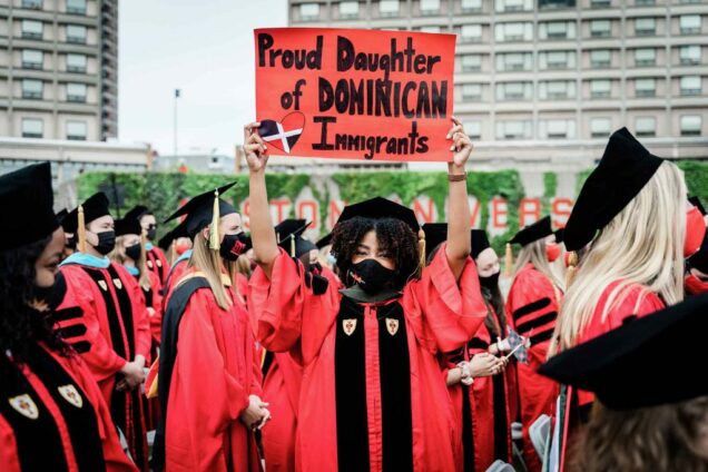 A graduating student holds a sign above her head that says 'Proud Daughter of DOMINICAN Immigrants' during the BU Commencement ceremony for advanced degrees.