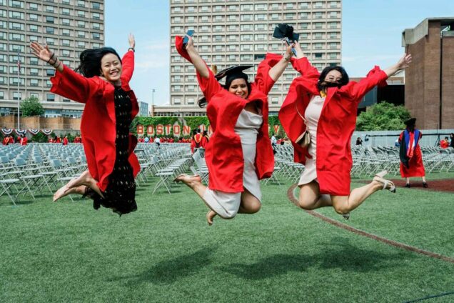 3 graduating students wearing caps and gowns jumping in the air on Nickerson Field.
