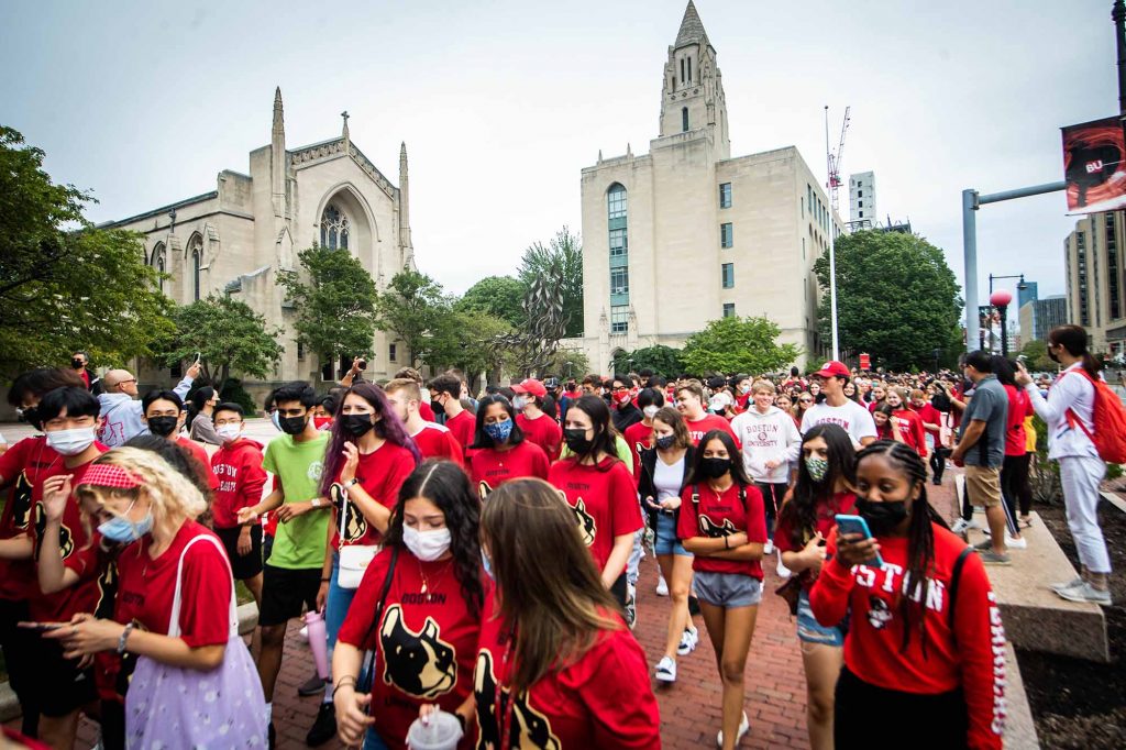 Groups of students, many in red BU shirts, marching in front of Marsh Plaza on their way to Matriculation at Agganis Arena.