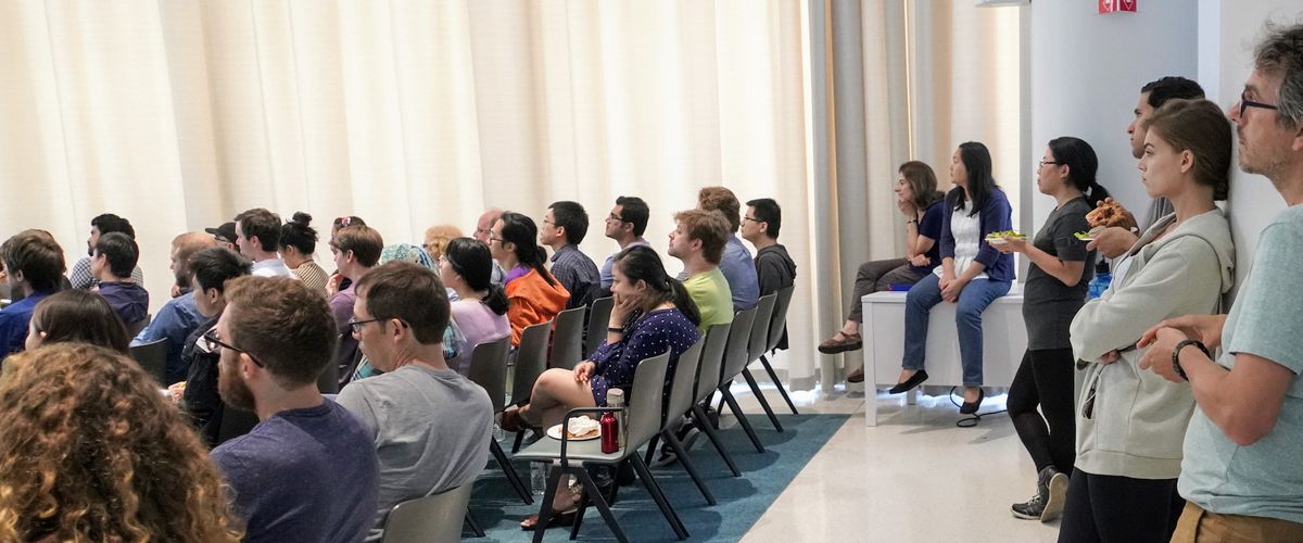 Audience attending a lecture, some are seated some are standing at the back of the auditorium